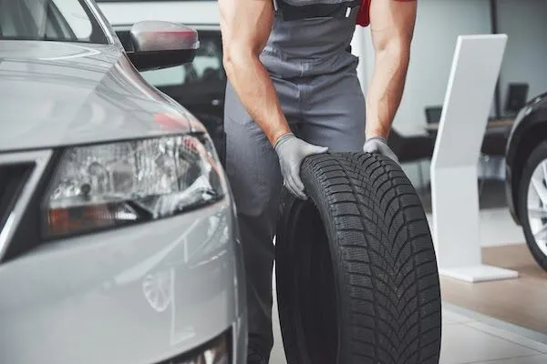 Auto mechanic holding car tire in auto repair shop